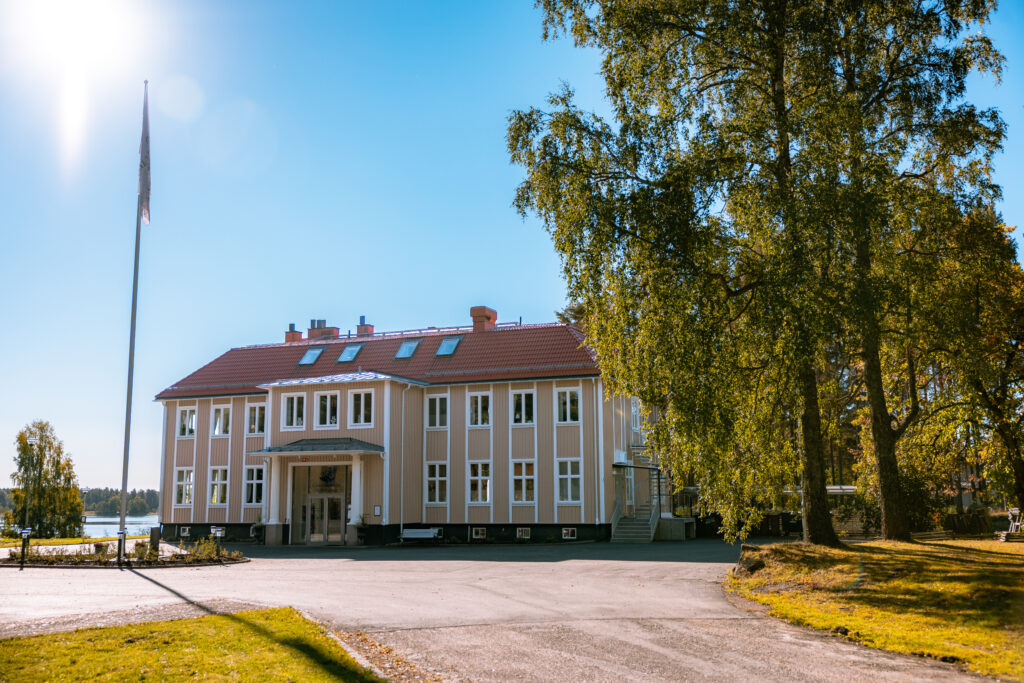 Ett stort gult hus mellan en flaggstång och två stora träd