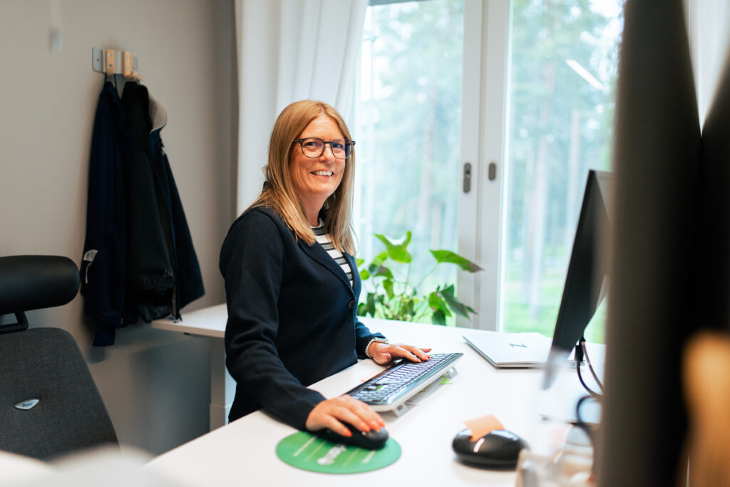 En kvinna står och ler vid sitt skrivbord